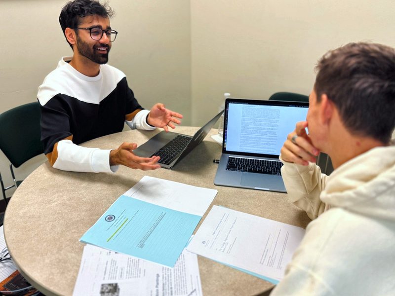 Saugat Bohara smiling as he talks a student through a reading assignment at a round table